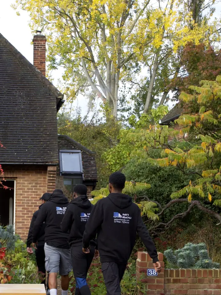 Three Pask's Removals London movers walking up a front garden path to a brick house in autumn