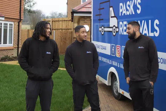 Three Pask's Removals London crew members in black uniforms beside the branded van at a new-build home