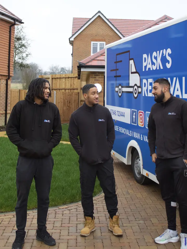 Three Pask's Removals London crew members in black uniforms beside the branded van at a new-build home