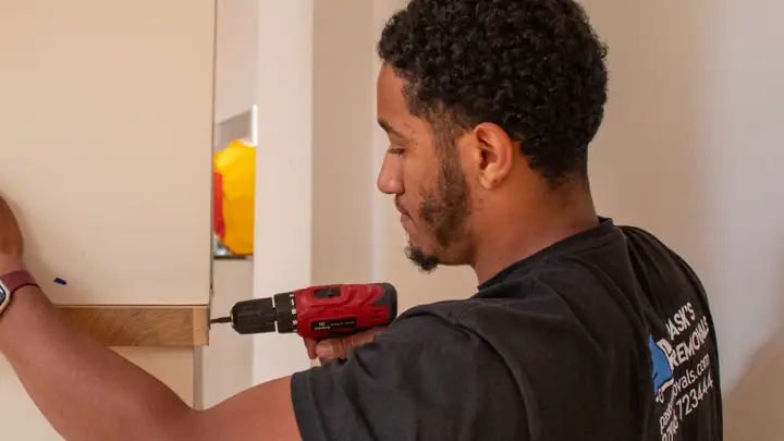 Pask's Removals London team member using a cordless drill on a wall inside a home