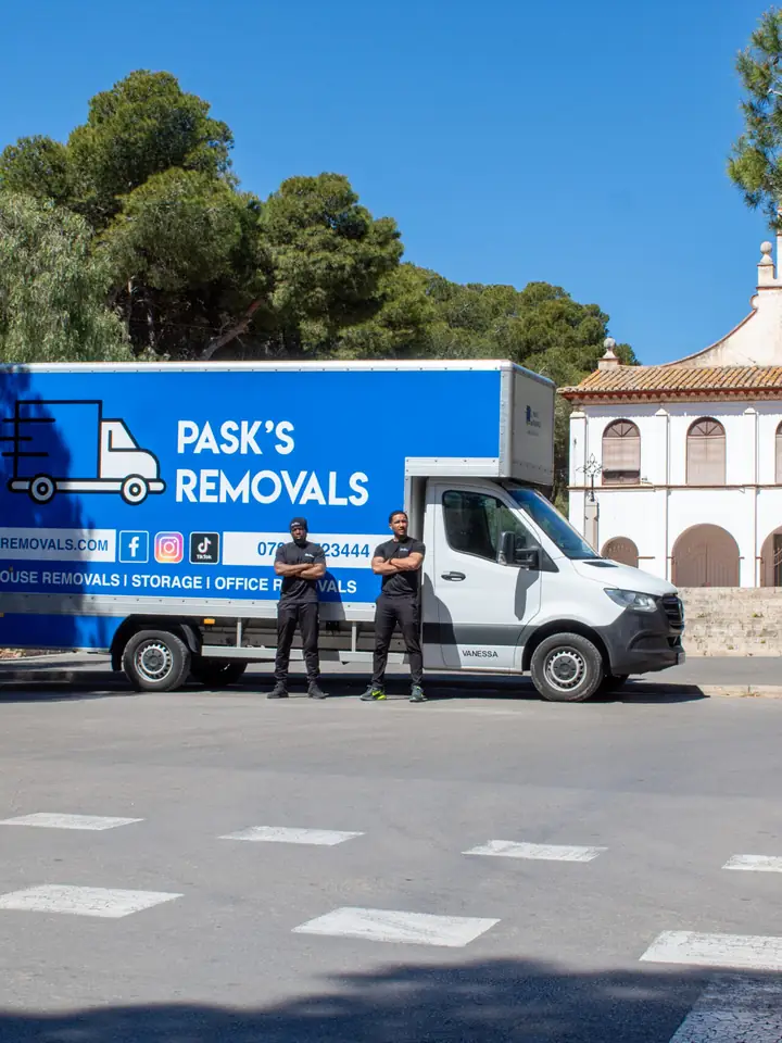 Pask's Removals London van and two crew in front of a white church on a sunny plaza