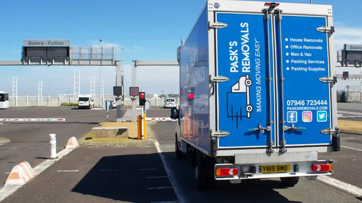 Rear of a Pask's Removals London van in a port check-in lane with French and English signs