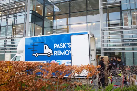 Pask's Removals London crew unloading boxes from the branded van outside a glass office building