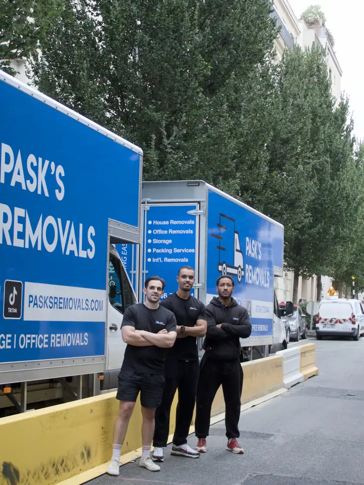 Three Pask's Removals London crew members beside branded removal vans on a tree-lined street
