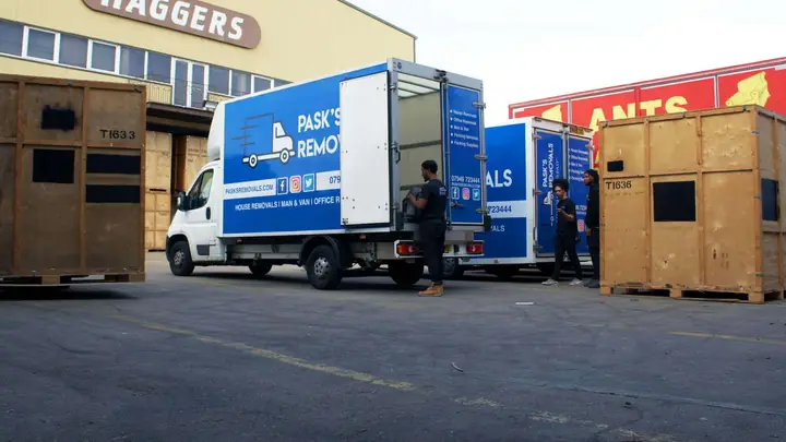 Pask's Removals London vans and crew in a warehouse yard lined with wooden storage containers
