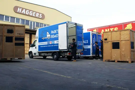 Pask's Removals London vans and crew in a warehouse yard lined with wooden storage containers